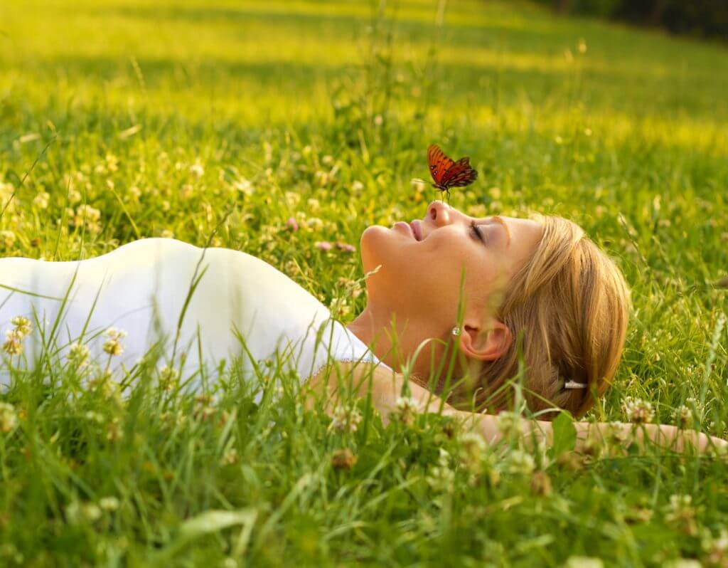 Young blond hair female lying down on grass.Butterfly standing on her nose.