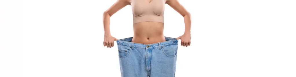 Hypnose-Abnehmen – sichtbarer Erfolg: schlanke Frau steht in viel zu großer Jeans nach Gewichtsverlust