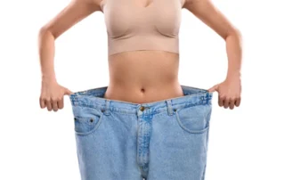 Hypnose-Abnehmen – sichtbarer Erfolg: schlanke Frau steht in viel zu großer Jeans nach Gewichtsverlust